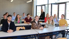 Gruppenfoto: Prof. Schmidt sitzt auf einem Tisch, um sie herum rund 15 Studierende