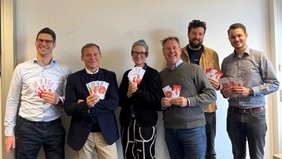 Six people smile at the camera and hold banknotes in their hands.