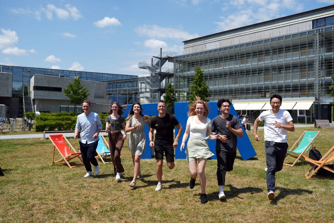 Studierende laufen auf der Campuswiese in einer Reihe Richtung Kamera