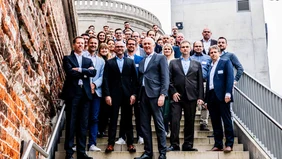 Ein Gruppenfoto auf einer Treppe, im Hintergrund Teile des brigk Gründerzentrums Ingolstadt.