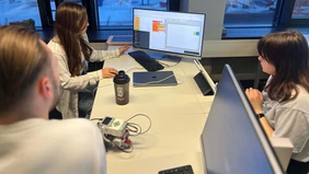 Mehrere Studierende sitzen um einen Computer und arbeiten zusammen an einer Programmierung.