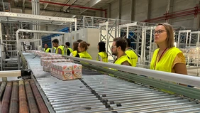 A group of people in yellow safety vests in front of a conveyor belt on which flour is being transported.