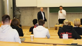 Two men in a lecture hall in front of a group of students