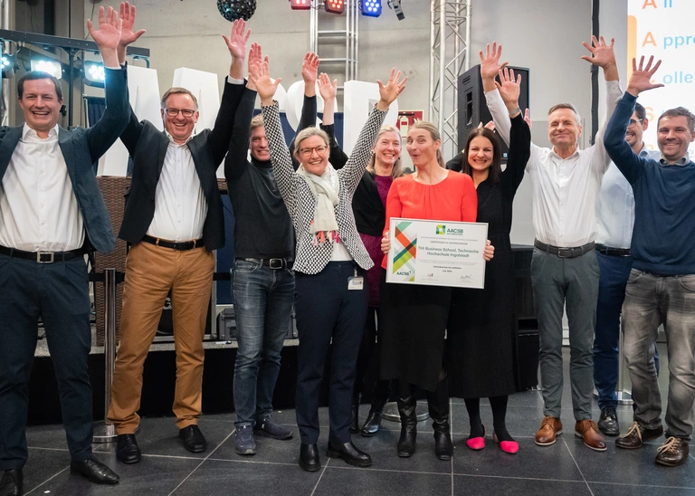 Ten cheering people, a woman in the middle holds up a certificate.