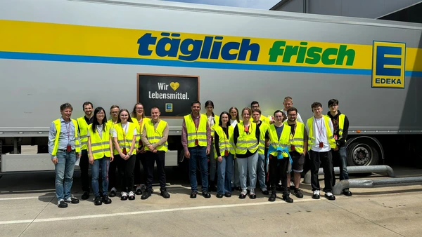 A group of people with yellow high-visibility vests in front of an Edeka truck.