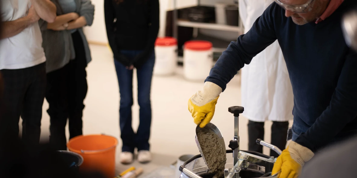 Laborversuch am Betonmischer, Mann mit Handschuhen füllt Zement ein
