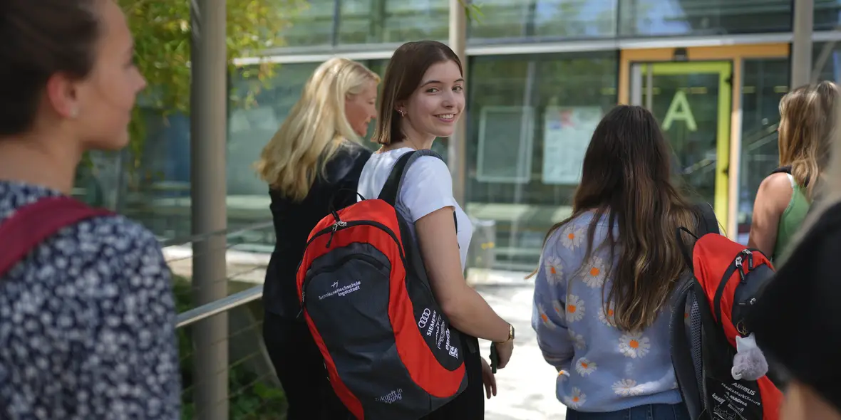 Studentin auf dem Weg Richtung THI Gebäude. Sie lächelt in die Kamera.